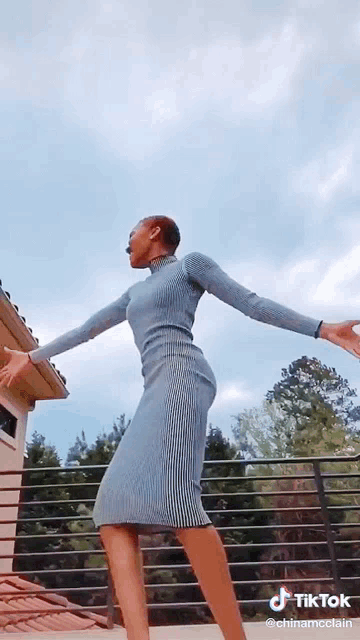 a woman in a blue dress is dancing on a balcony with a tiktok watermark at the bottom