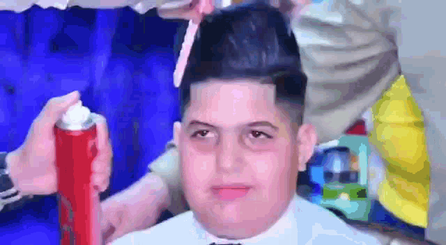 a young man is getting his hair cut by a barber while holding a can of hairspray .