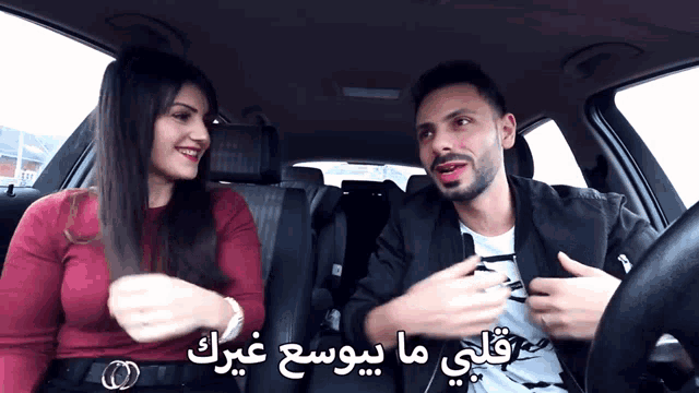 a man and a woman are sitting in a car with arabic writing behind them