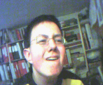 a young man wearing glasses is smiling in front of a bookcase