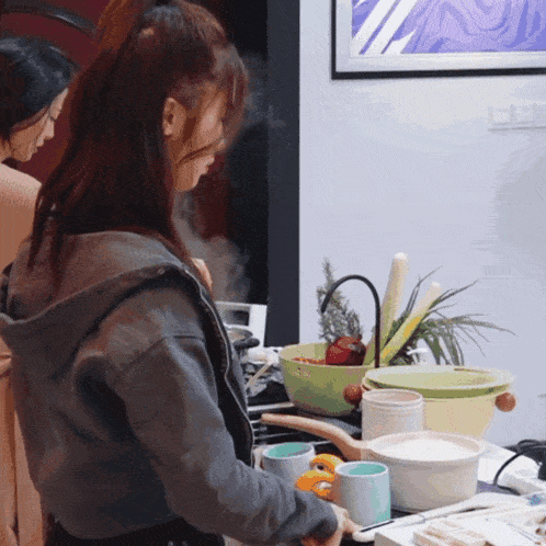 a woman cooking in a kitchen with a picture on the wall behind her