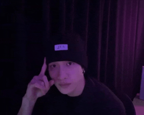 a man wearing a black beanie is sitting in front of a purple curtain and making a funny face .