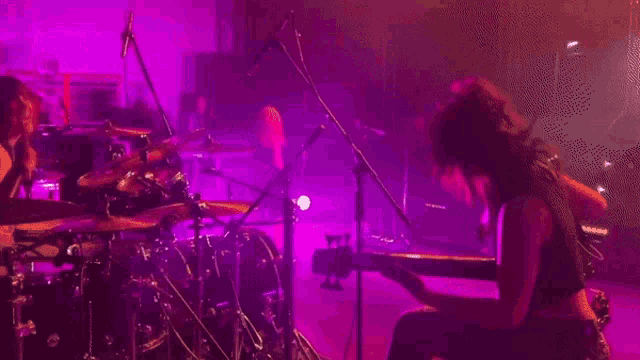 a man playing drums and a woman playing a keyboard in a dark room with purple lights