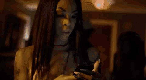 a person is holding a cell phone in their hand while another person looks on .