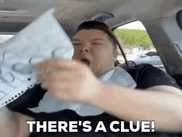 a man is sitting in a car holding a piece of paper and saying `` there 's a clue . ''