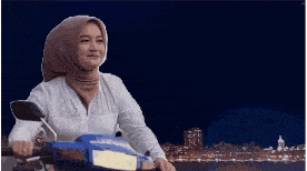 a woman wearing a hijab is sitting on a scooter at night