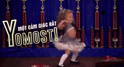 a little girl in a tutu is dancing on a stage in front of trophies