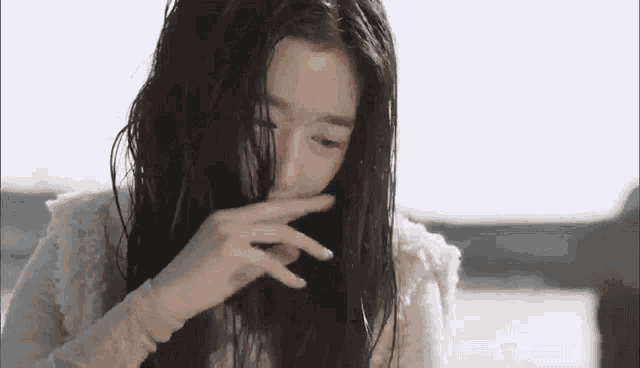 a woman with long hair is covering her face with her hand .