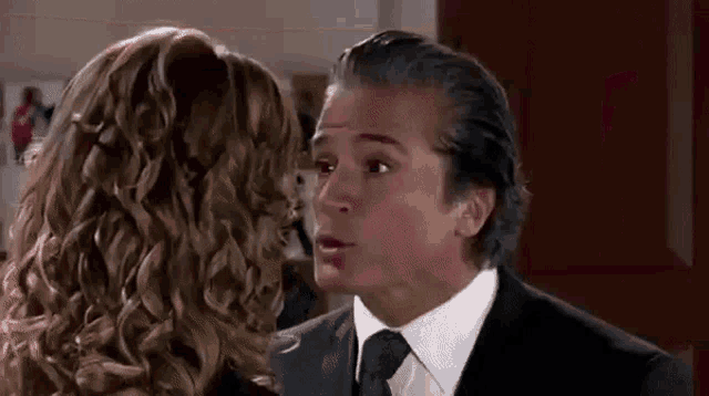 a man in a suit and tie is kissing a woman on the forehead .