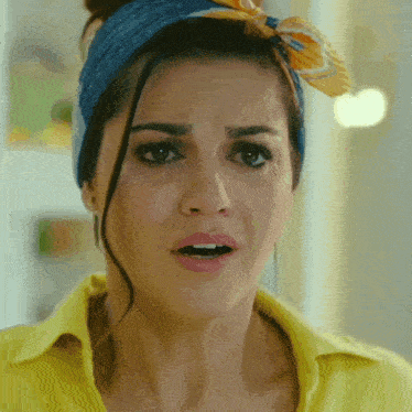a woman wearing a yellow shirt and a blue headband making a surprised face