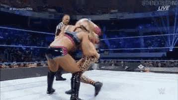 two women are wrestling in a wrestling ring with a referee in the background .