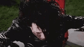 a man in a black leather jacket is standing in the rain with a tear coming out of his eye .