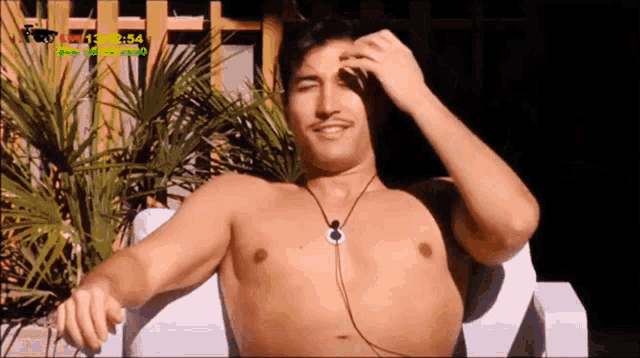 a man without a shirt is sitting on a white chair with the time of 13:54