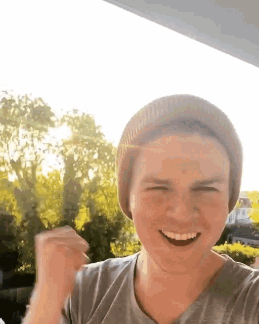 a young man wearing a beanie and a gray shirt is smiling