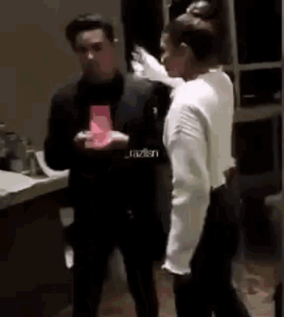a man and a woman are standing next to each other in a room . the woman is holding a red envelope .