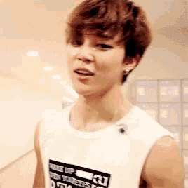 a young man with brown hair is wearing a white tank top and earrings .