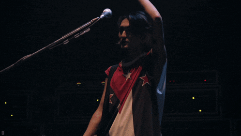 a man is singing into a microphone with a red white and blue shirt on