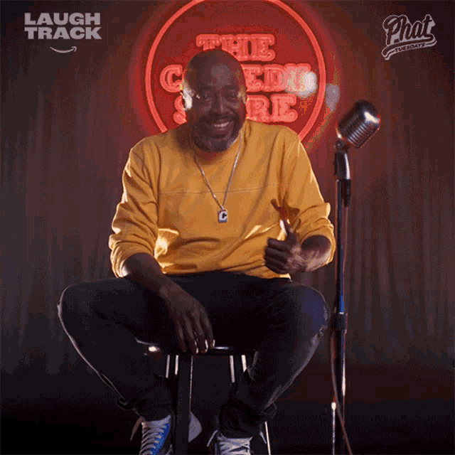 a man sits on a stool in front of a laugh track sign