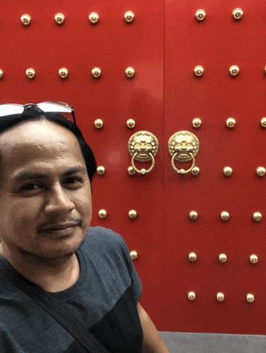 a man wearing sunglasses stands in front of a red door with gold knobs