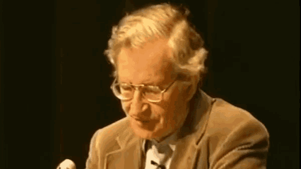 a man wearing glasses is speaking into a microphone in a dark room
