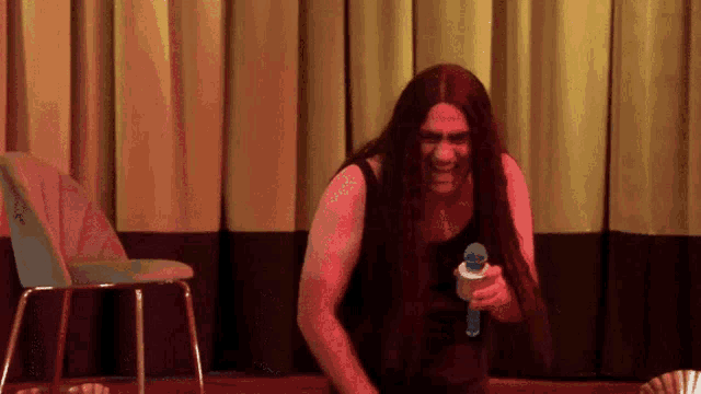 a man with long hair is holding a microphone in front of a chair