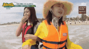 two women are standing on a beach and one is wearing a life vest