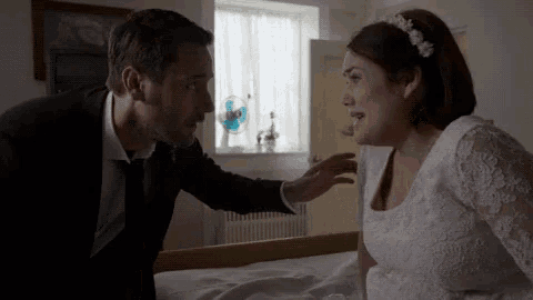 a man in a suit and tie talks to a woman in a white dress