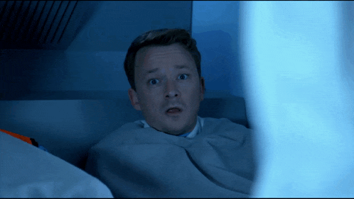 a man with a surprised look on his face is laying under a blanket