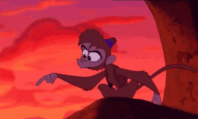 a monkey is sitting on top of a rock pointing at something .