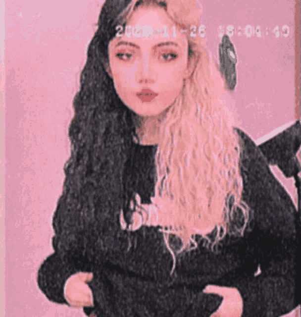 a woman with long hair and red lips is standing in front of a pink background .