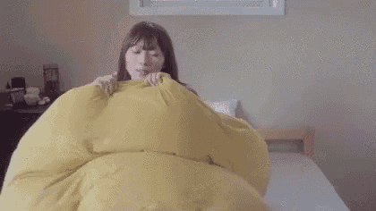 a woman is laying on a bed with a yellow blanket and covering her face with her hand .