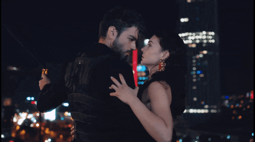 a man and a woman are hugging in front of a city skyline at night