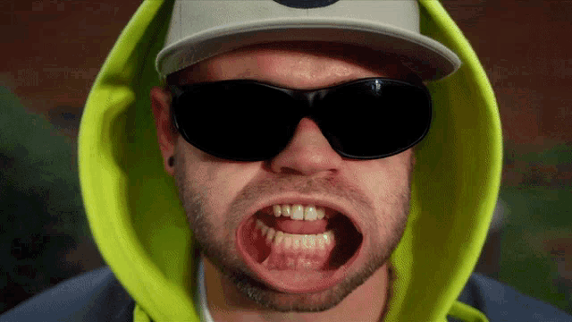 a man wearing sunglasses and a yellow hoodie shows his teeth