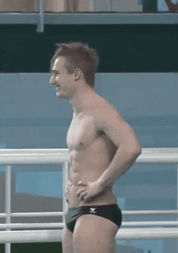 a shirtless man in black swim trunks is standing in front of a fence .