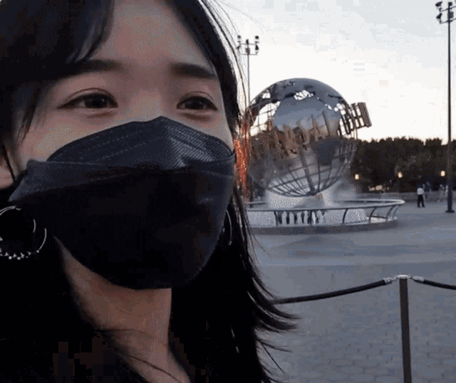 a woman wearing a black face mask stands in front of a large globe that says universal