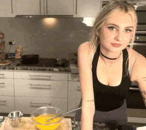 a woman in a black tank top stands in a kitchen next to a bowl of yellow liquid