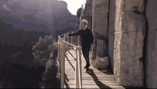 a man is walking across a wooden bridge between two cliffs .