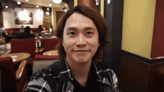 a young man in a plaid shirt is smiling in a cafe