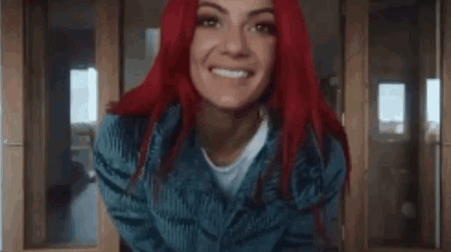 a woman with red hair is smiling and wearing a blue sweater and a white shirt .