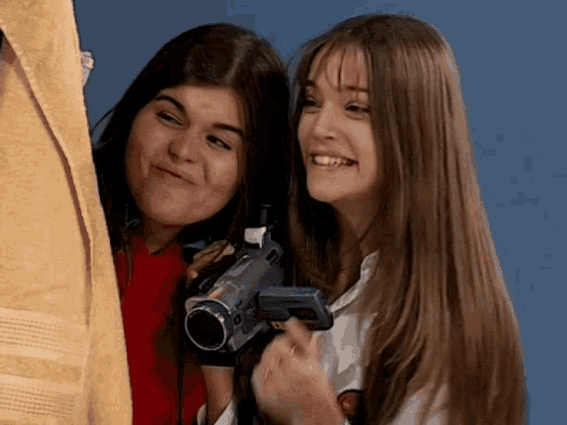 two girls are standing next to each other one is holding a video camera and the other is holding a towel