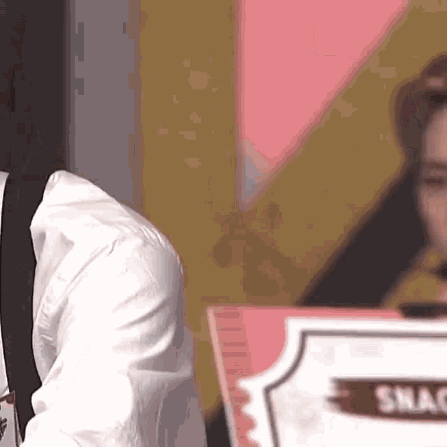 a man in a white shirt and black suspenders is sitting at a table with a sign that says shack .