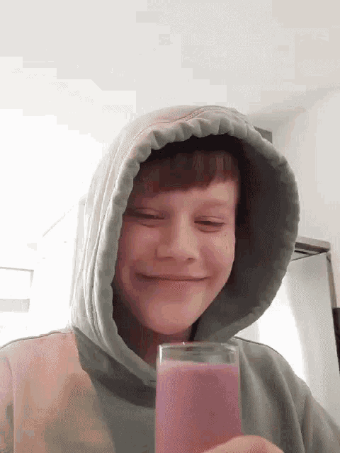 a young boy wearing a hooded sweatshirt is holding a glass of pink liquid