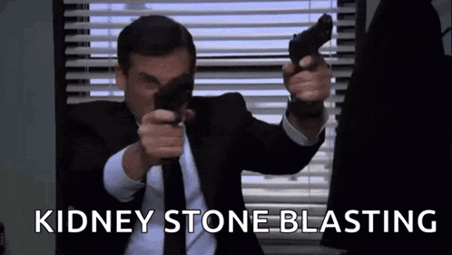 a man in a suit and tie is pointing two guns at the camera while sitting in front of a window .