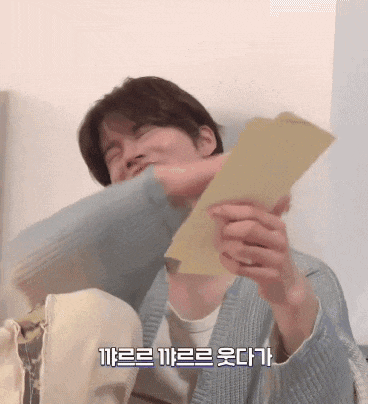 a man in a blue sweater is holding a piece of paper with korean writing on it .