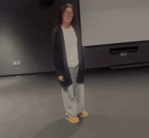 a woman wearing glasses and a cardigan is standing in a dark room
