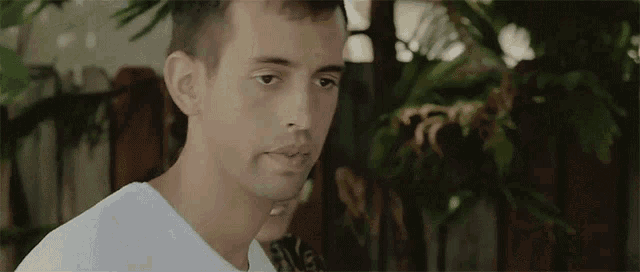 a man in a white shirt is standing in front of a wooden fence