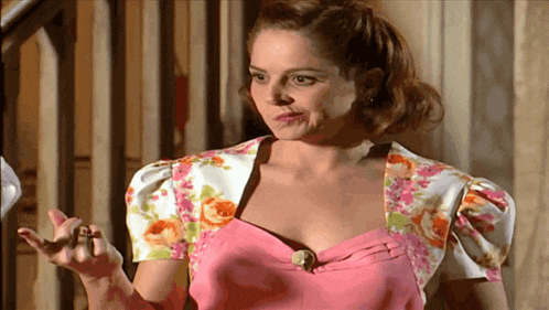 a woman in a pink dress and floral jacket is making a face