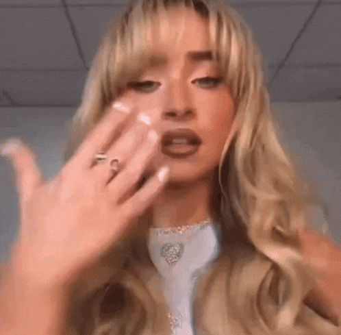 a woman with long blonde hair and a ring on her finger is making a funny face .