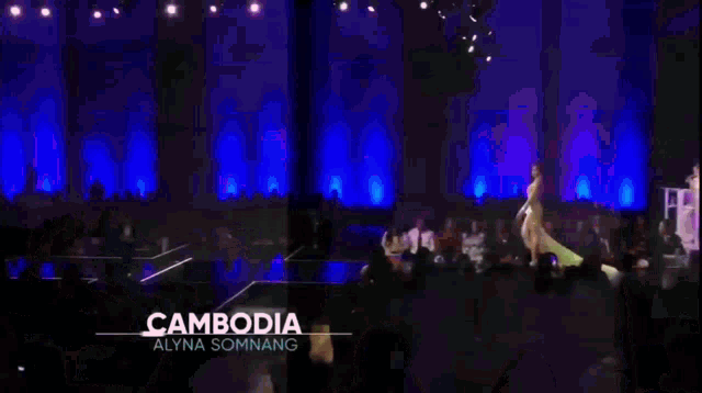 a woman wearing a green dress and a sash that says cambodia is walking down a runway .