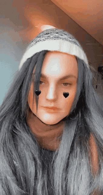 a woman wearing a beanie and a scarf has two black hearts on her face
